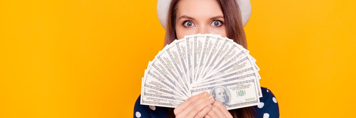 A young woman wearing a hat holds a fan of hundred dollar bills.