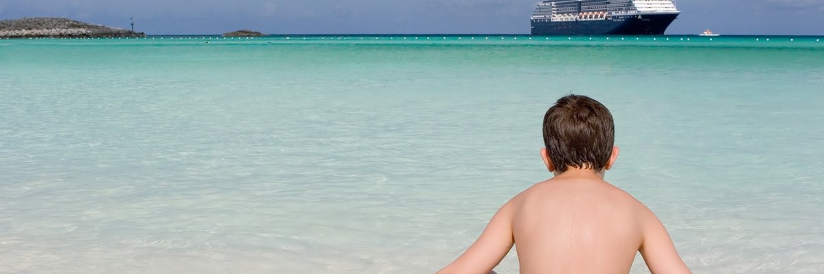 Child on shore of beach with cruise ship off in the distance.