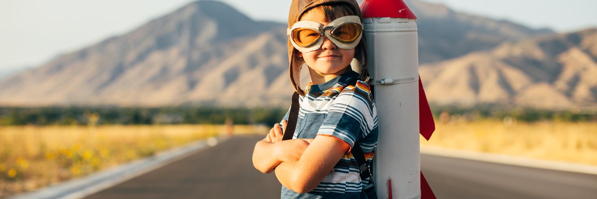 Child standing on a rural road with a toy rocket ship strapped to his back