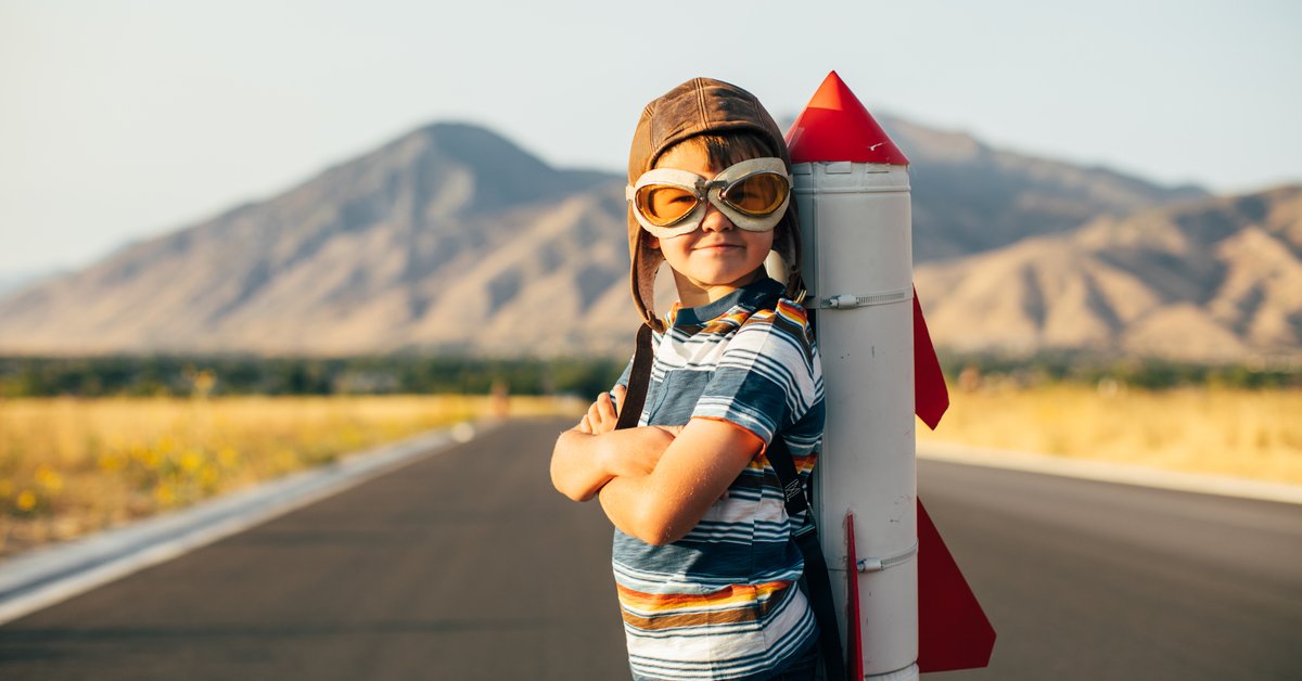 Child standing on a rural road with a toy rocket ship strapped to his back