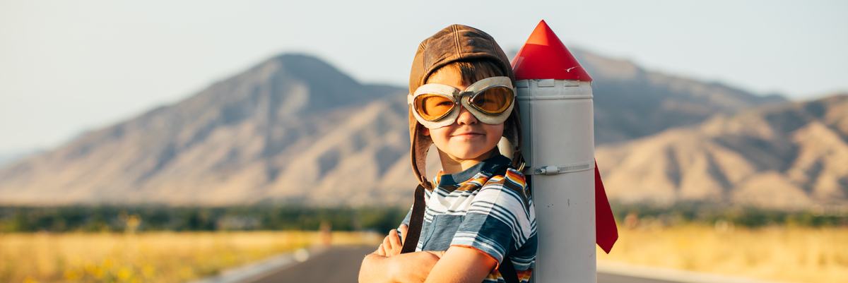 Child standing on a rural road with a toy rocket ship strapped to his back