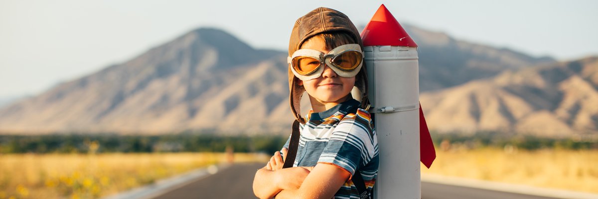Child standing on a rural road with a toy rocket ship strapped to his back