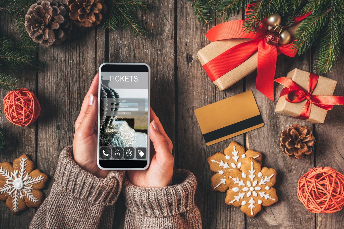 Christmas decor and a credit card on a table around hands holding a phone showing a ticket purchase screen.