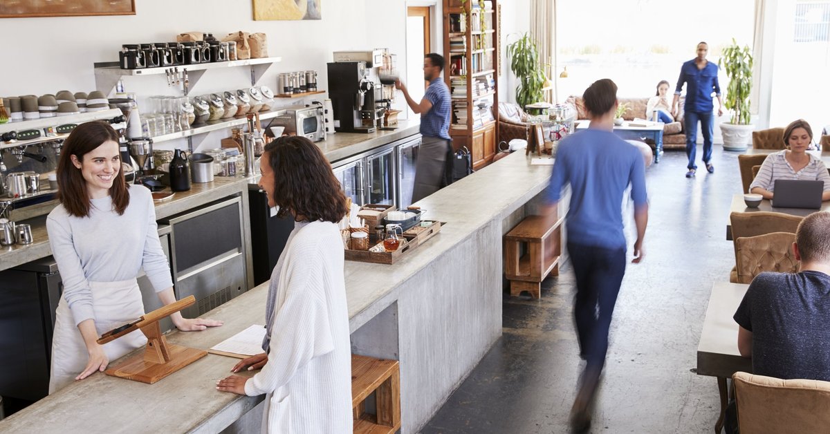 A busy coffee shop with a woman paying at the register.