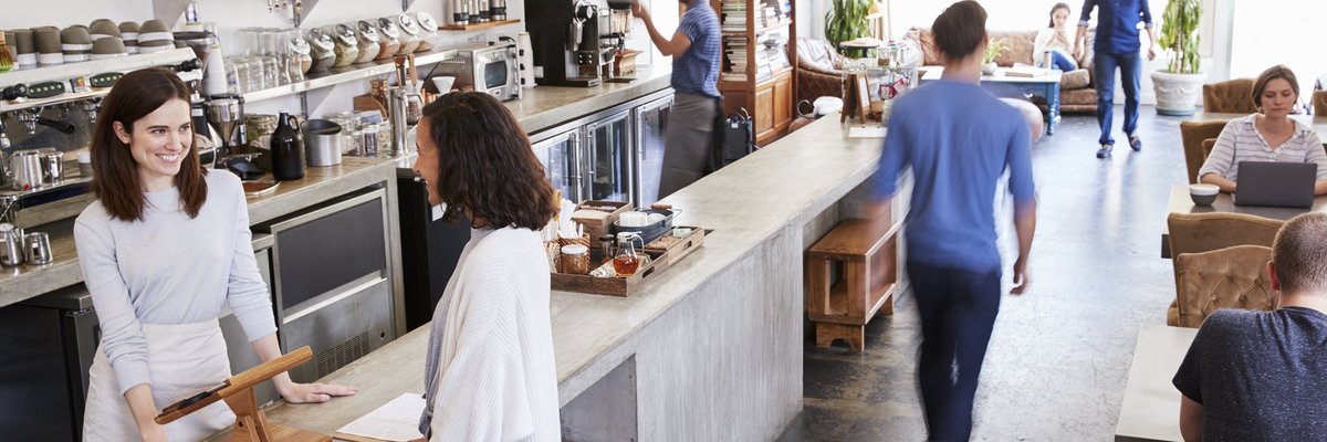 A busy coffee shop with a woman paying at the register.