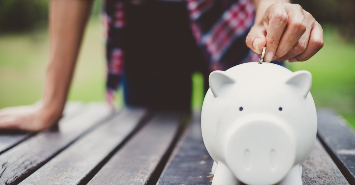 A person putting a coin in a piggy bank on a picnic table.