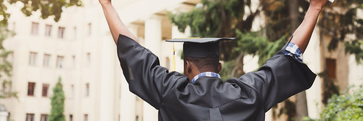 A person holding a diploma and wearing graduation robes celebrates.