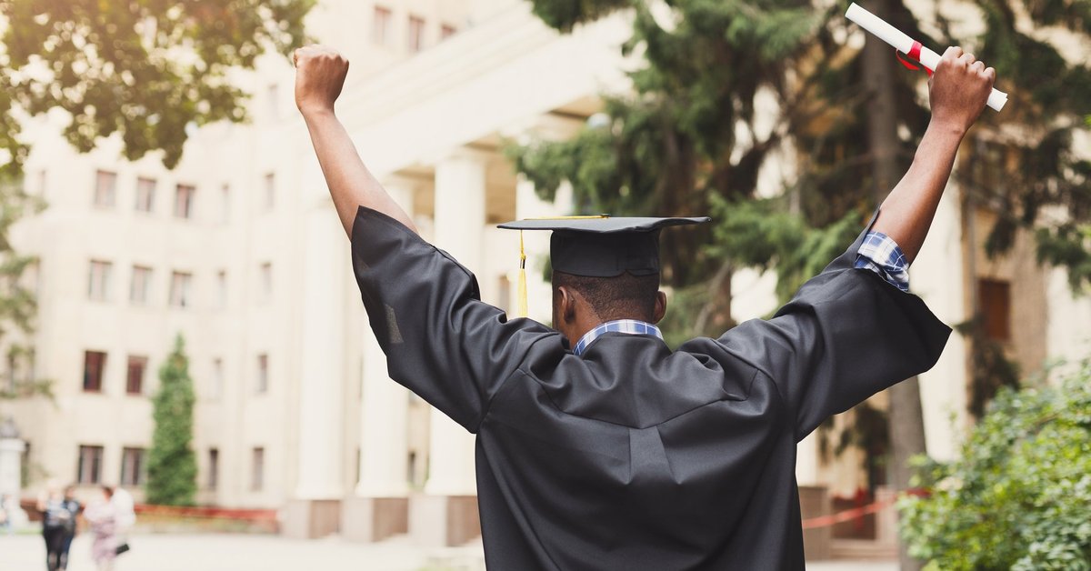 A person holding a diploma and wearing graduation robes celebrates.