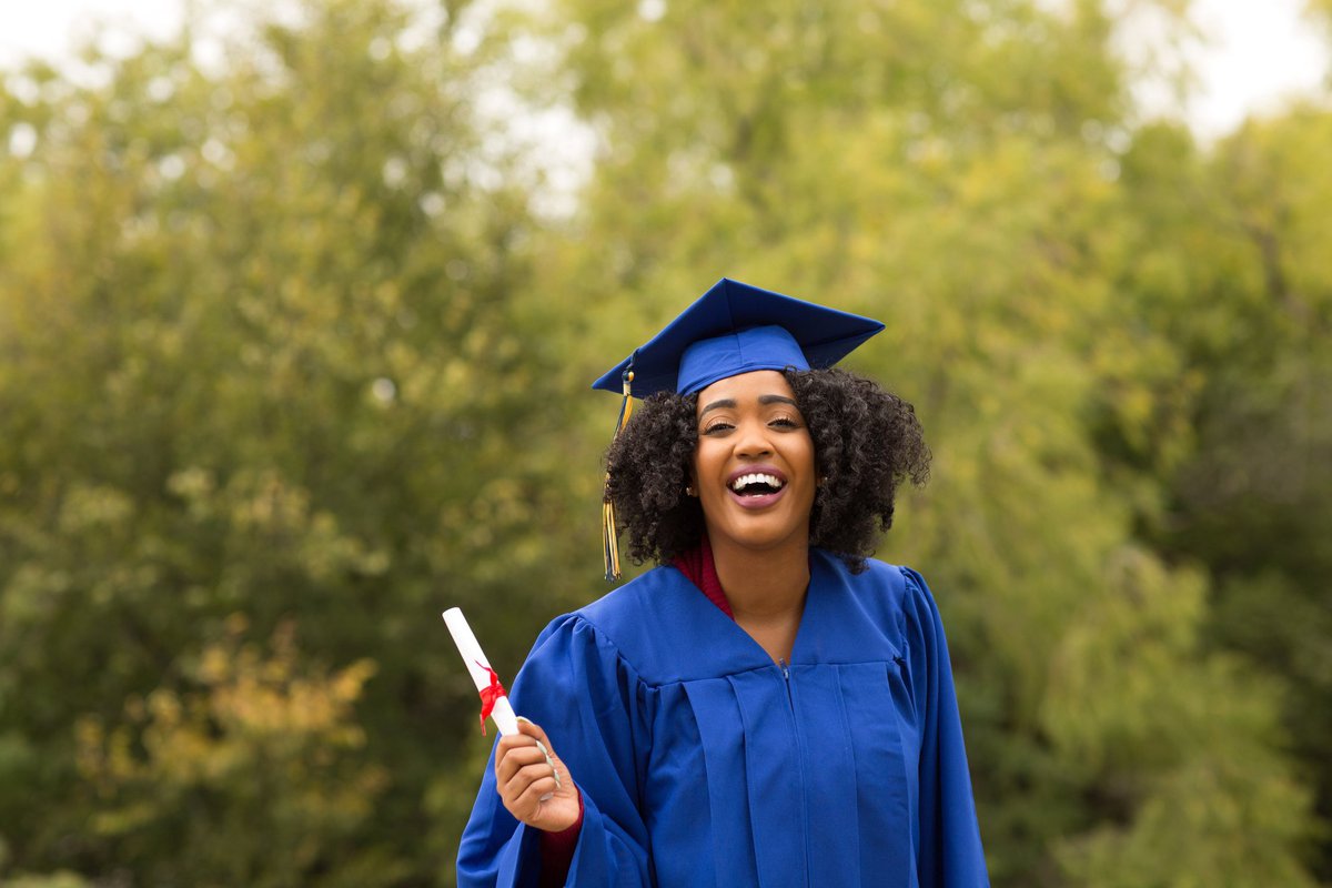 A woman smiling in a college graduation cap and gown.