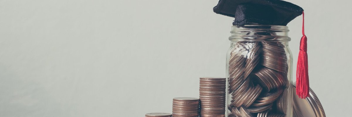 Stacks of coins leading up to a jar of coins with a mortarboard on top