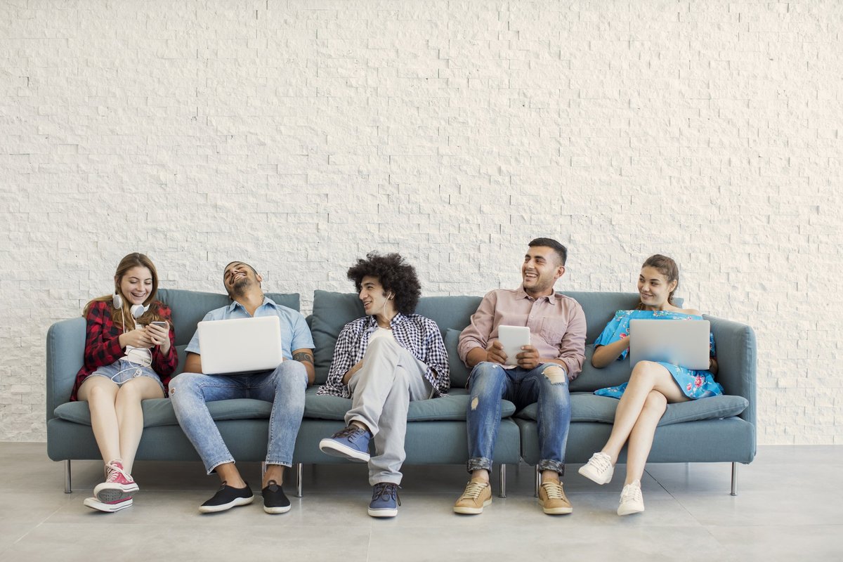 Un groupe d'amis d'âge universitaire sur un canapé avec des ordinateurs portables ou des téléphones.