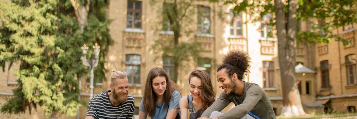 College students studying on the grass in front of a large school building.