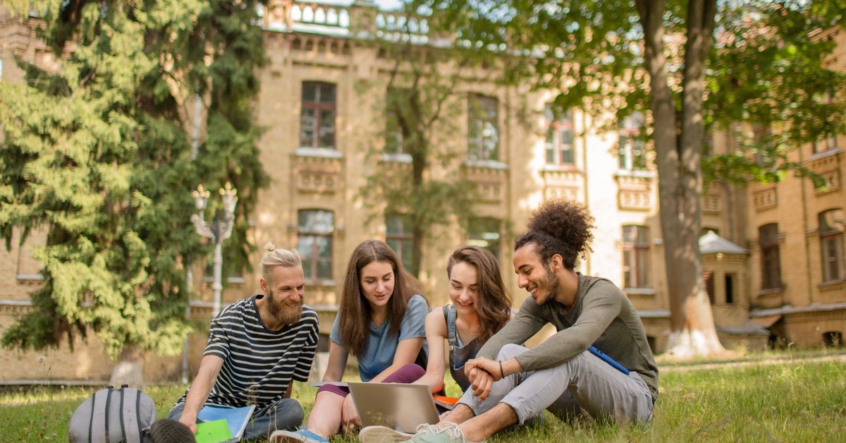 College students studying on the grass in front of a large school building.