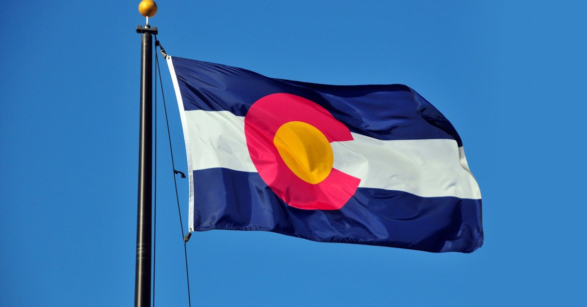 The Colorado state flag fluttering in front of a blue sky.
