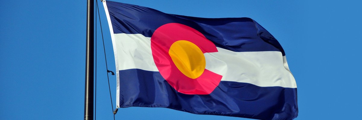 The Colorado state flag fluttering in front of a blue sky.