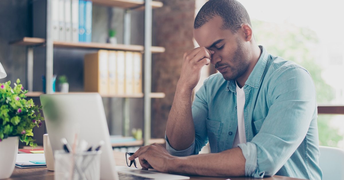 Stressed man sitting in front of laptop with his hand on his face