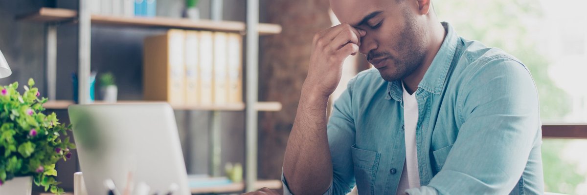 Stressed man sitting in front of laptop with his hand on his face