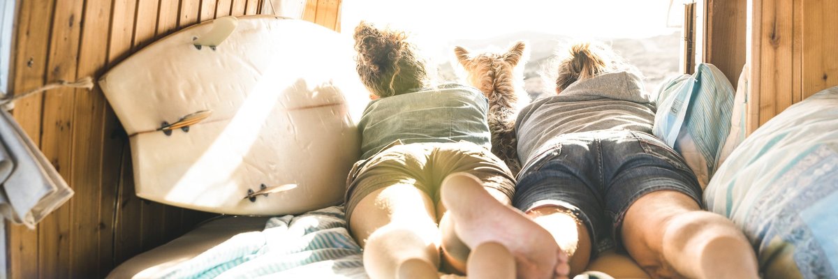 Young couple lying in RV with dog looking out over mountains