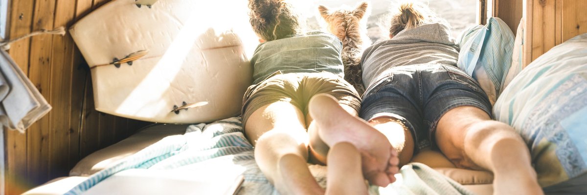 Young couple and their dog lying in a camper van next to a surfboard.