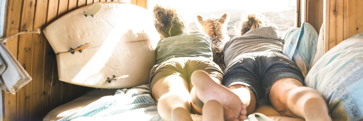 Young couple lying in RV with dog looking out over mountains