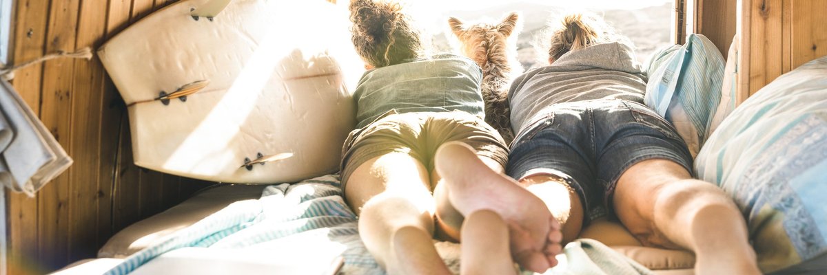 Young couple lying in RV with dog looking out over mountains