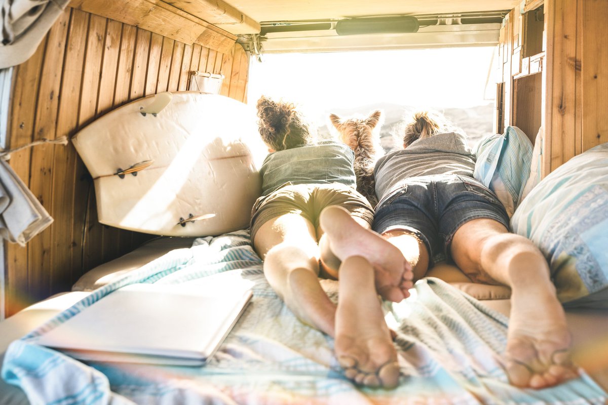 Young couple lying in RV with dog looking out over mountains