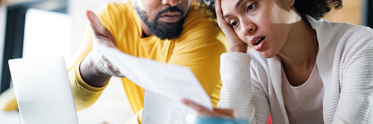 Couple appears frustrated while looking at paperwork over laptop.