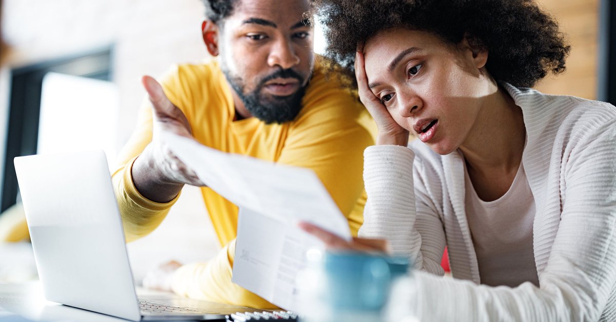 Couple appears frustrated while looking at paperwork over laptop.