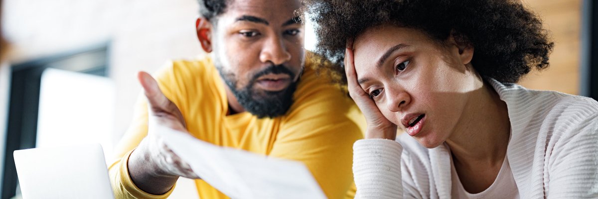Couple appears frustrated while looking at paperwork over laptop.