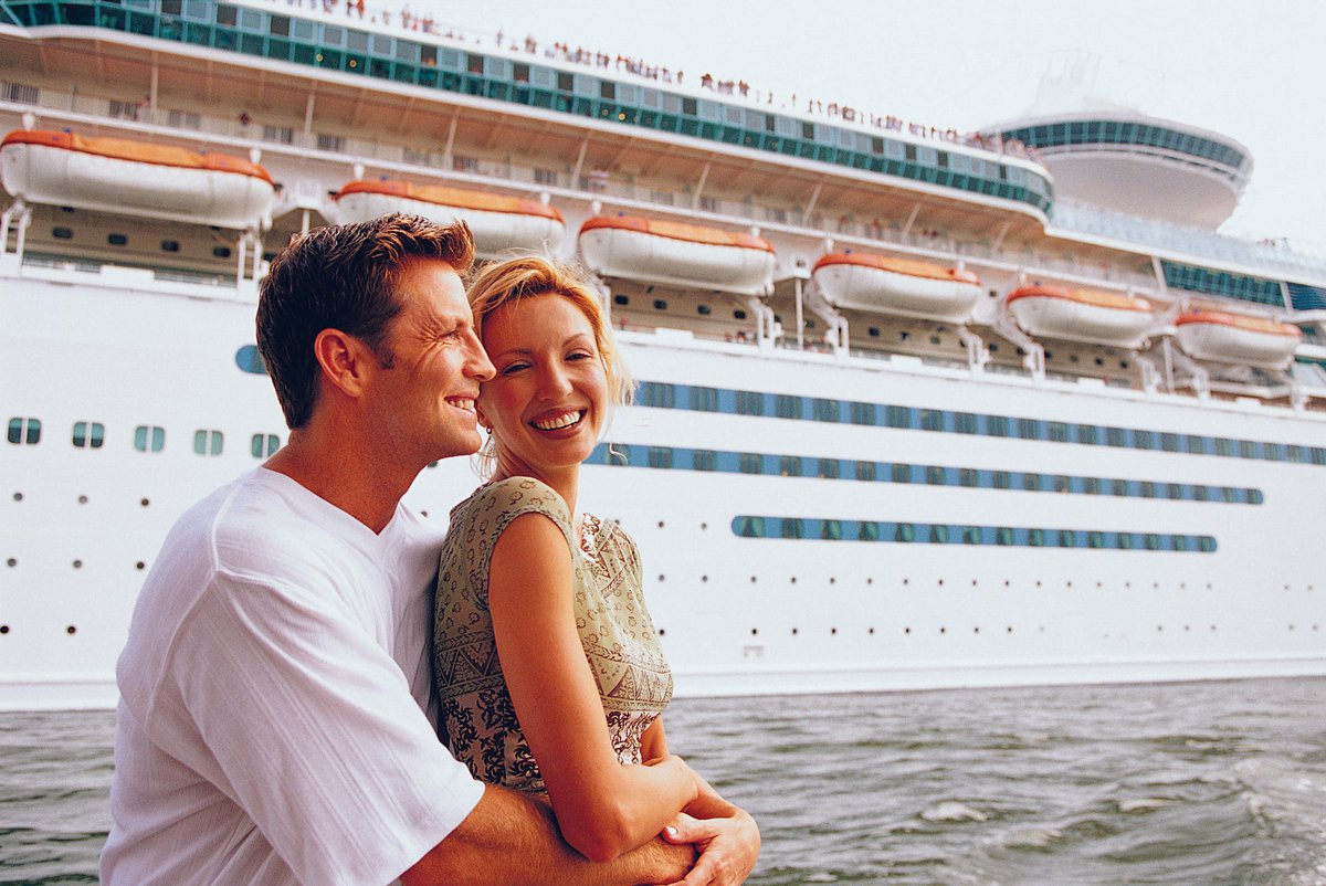 Couple embracing in front of cruise ship.