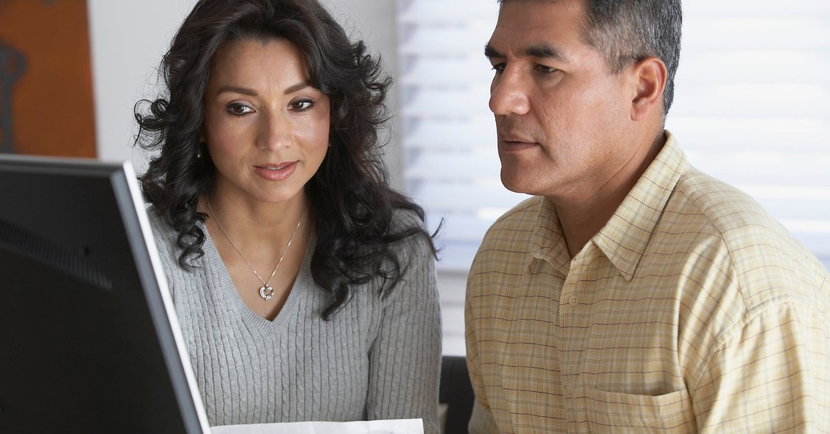 Couple holding a document and looking at a computer screen together.