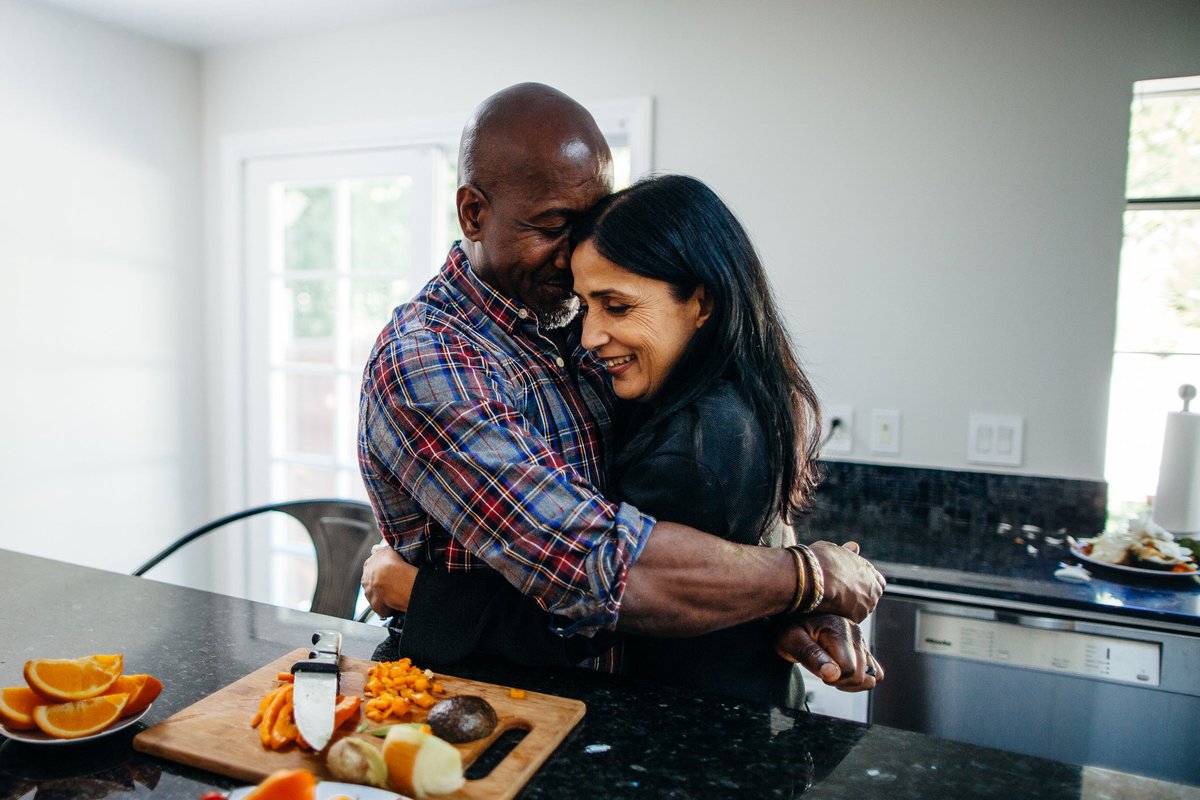 Couple hugging in kitchen while preparing food.
