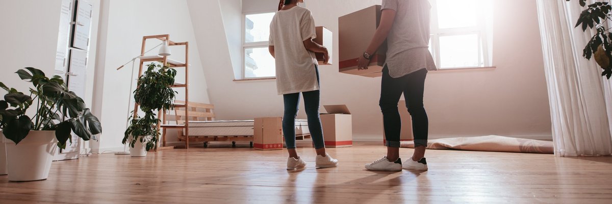 A young couple moving boxes and plants into a new apartment.