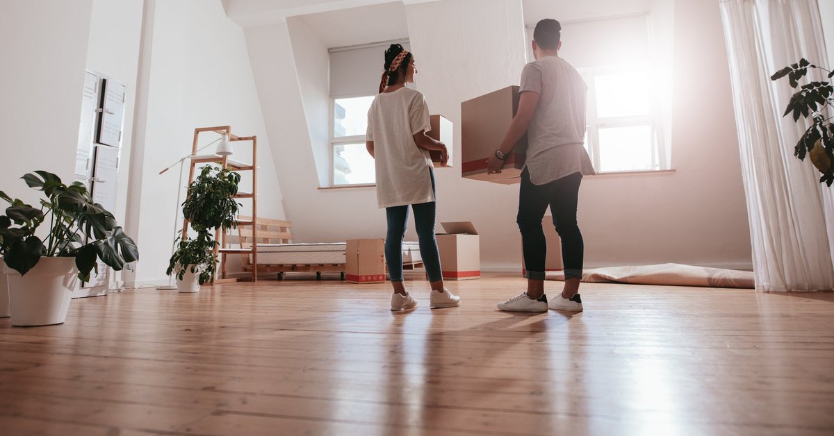 A young couple moving boxes and plants into a new apartment.