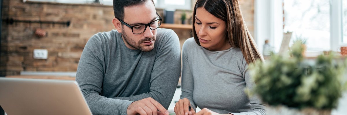 A couple paying their bills at a table with a laptop and notebook.