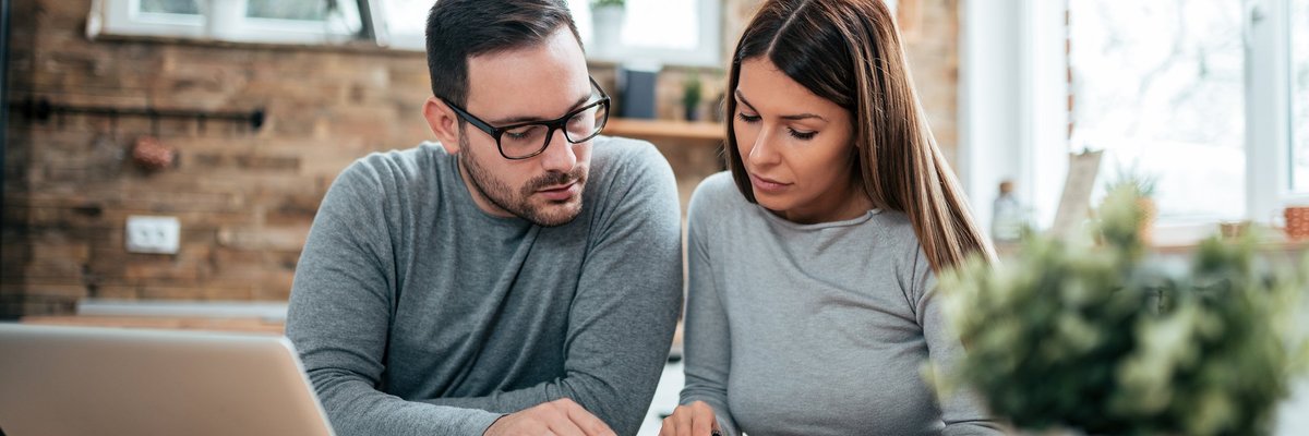 A couple paying their bills at a table with a laptop and notebook.