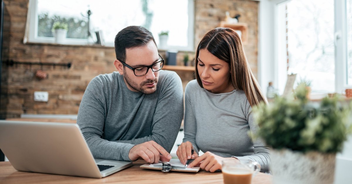 A couple paying their bills at a table with a laptop and notebook.