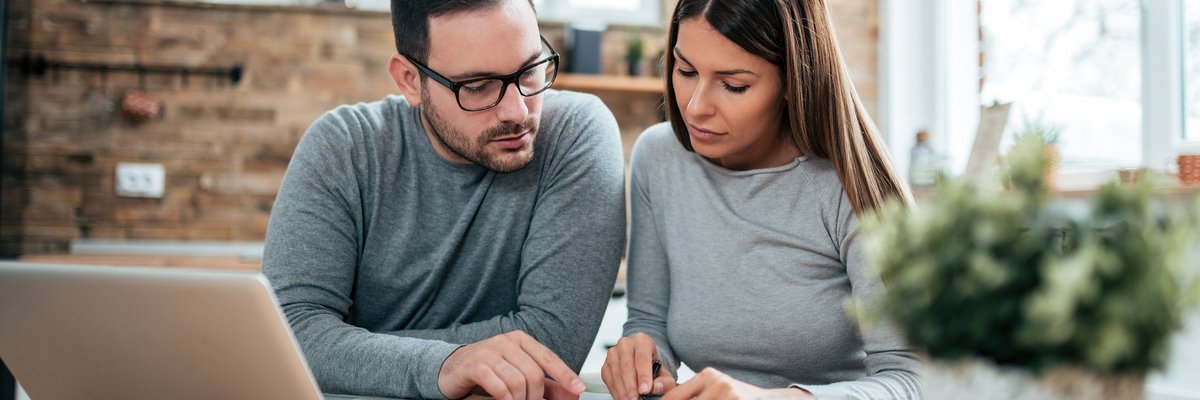 A couple paying their bills at a table with a laptop and notebook.