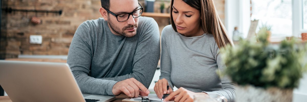 A couple paying their bills at a table with a laptop and notebook.