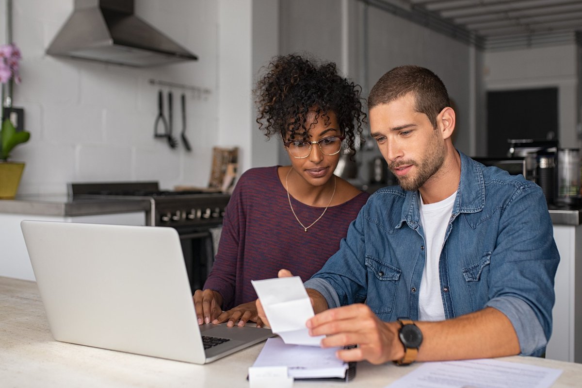 A young couple looking though paperwork in front of a laptop.