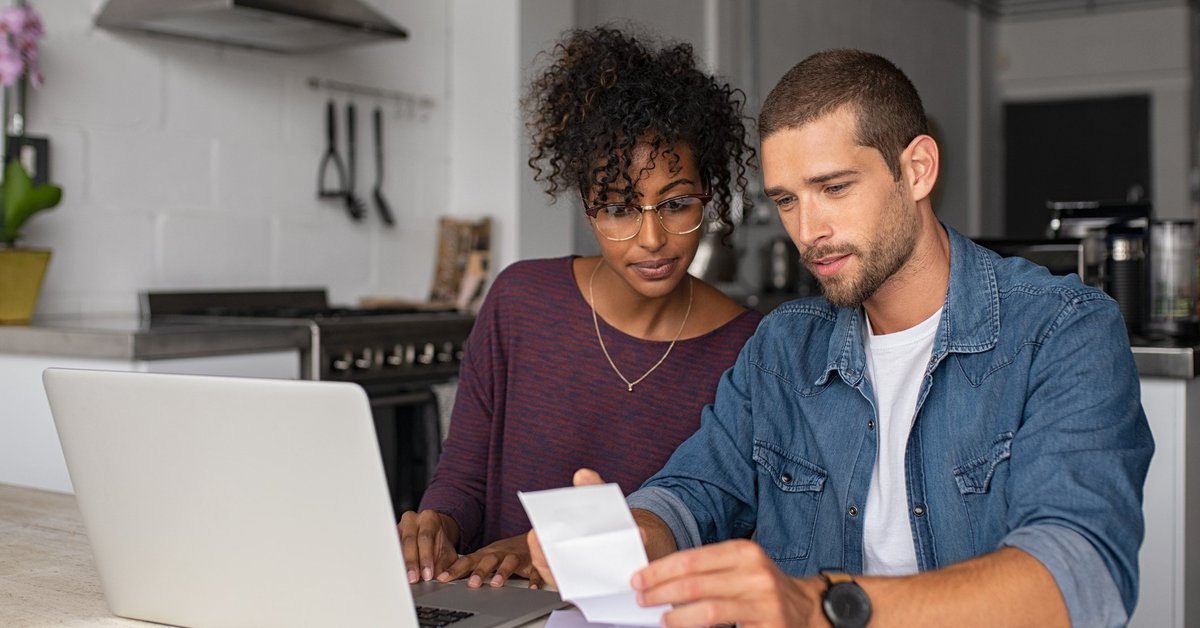 A young couple paying bills at their kitchen table.