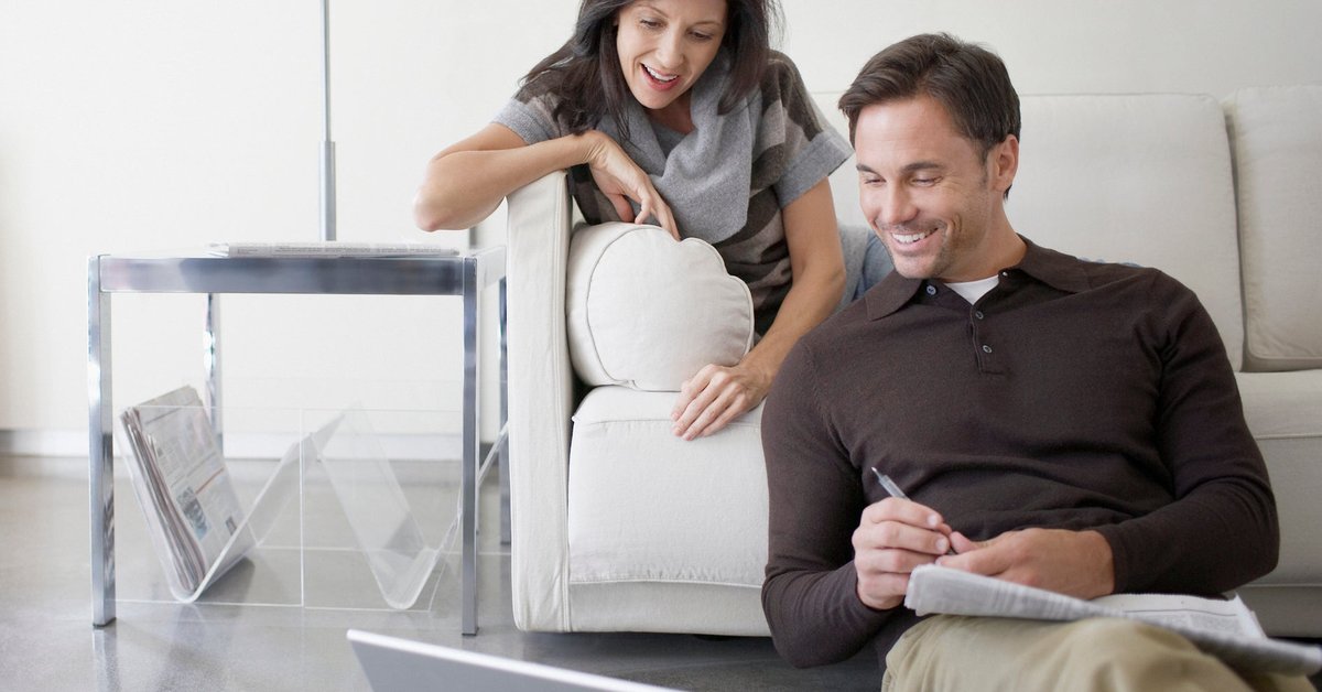 A couple relax at home, reading the news on a laptop.