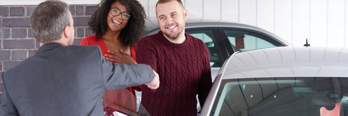 Couple shakes hand with a car salesman near a vehicle for sale.