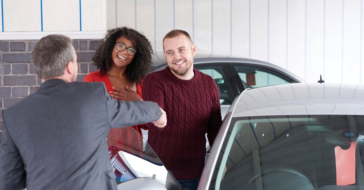 Couple shakes hand with a car salesman near a vehicle for sale.