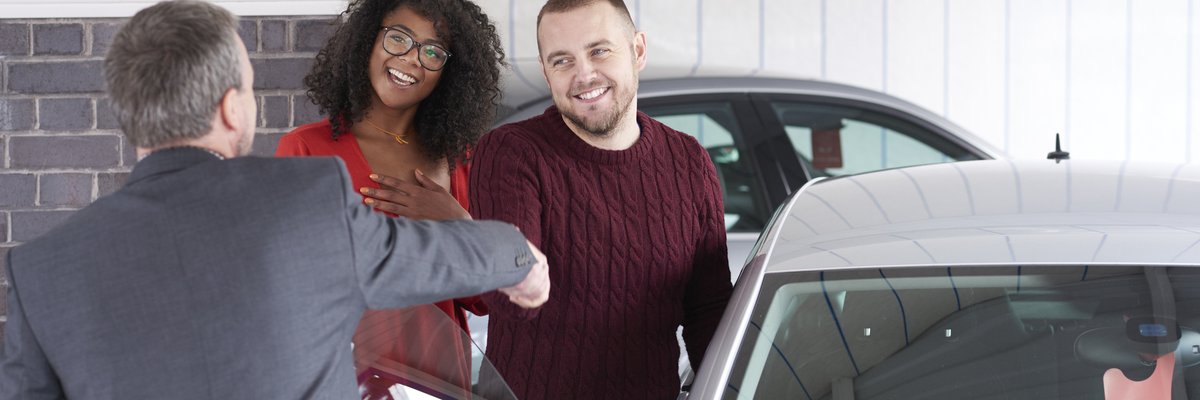 Couple shakes hand with a car salesman near a vehicle for sale.