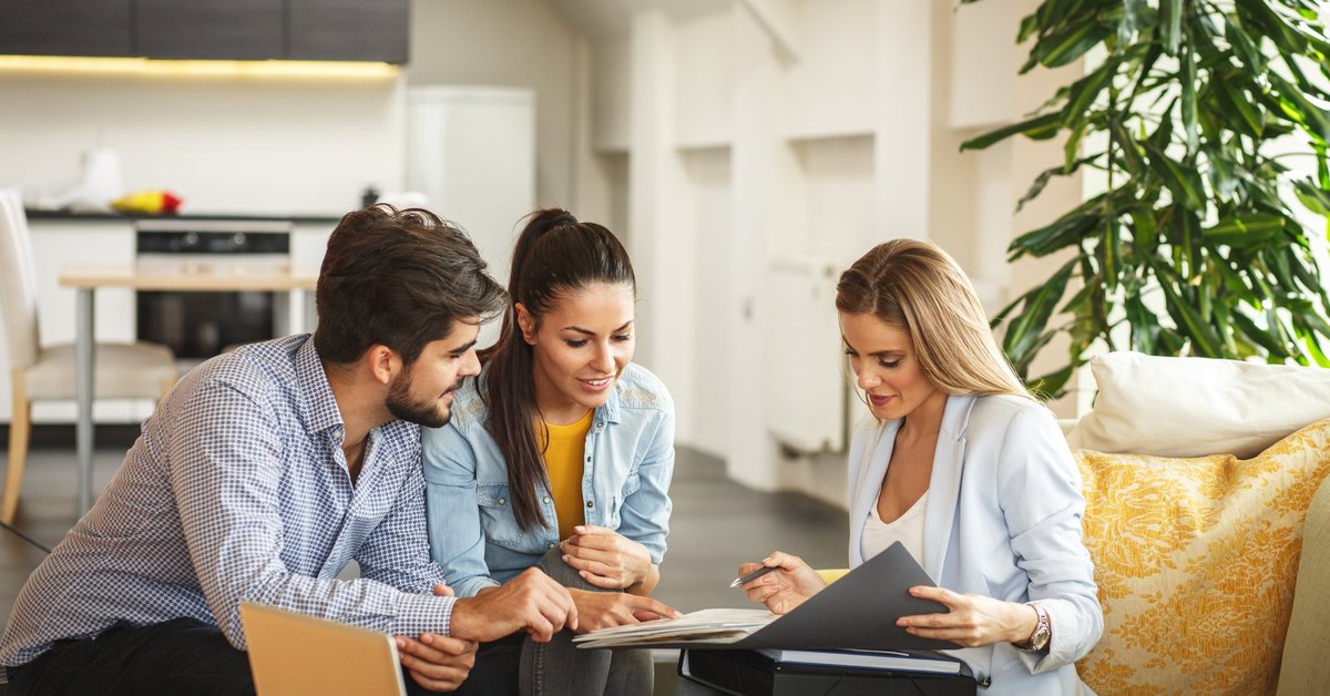 A couple signing paperwork with a realtor in a new house.