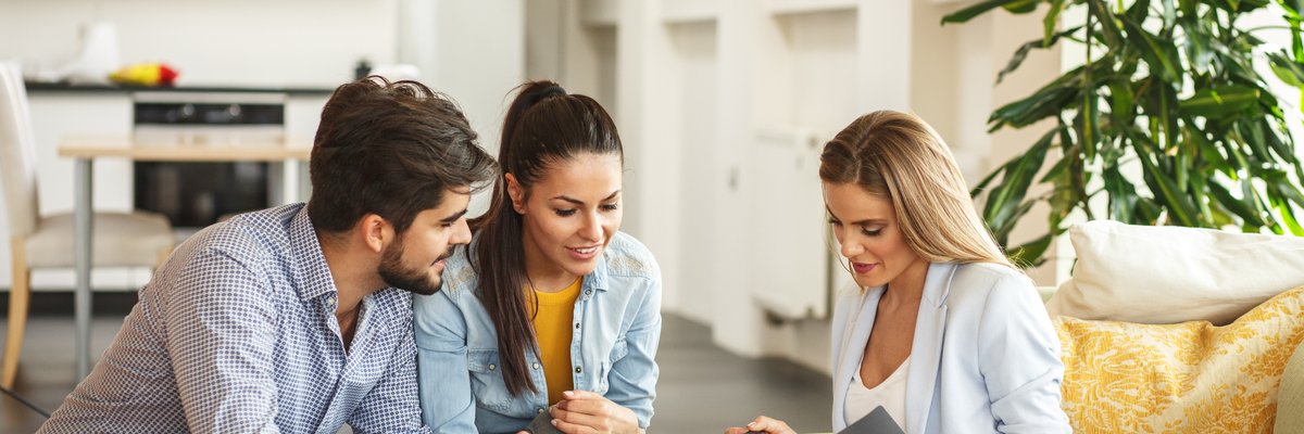 A couple signing paperwork with a realtor in a new house.