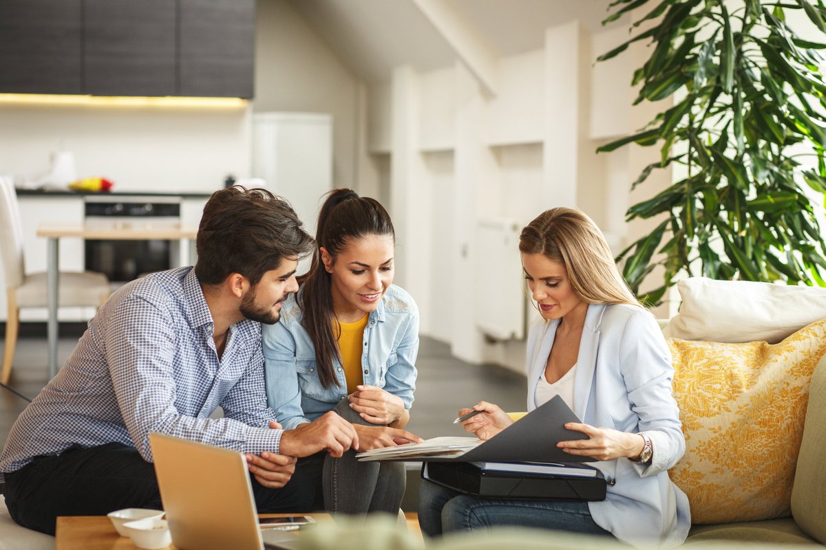 A couple signing paperwork with a realtor in a new house.