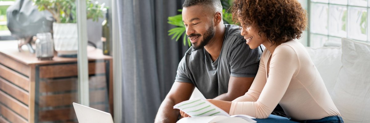 A couple sit in their living room and pay their credit card balances online.