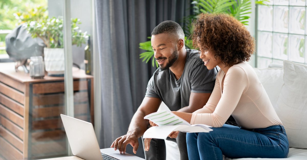 A couple sit in their living room and pay their credit card balances online.